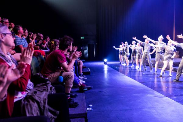 Circus performers waiving hands, audience clapping.