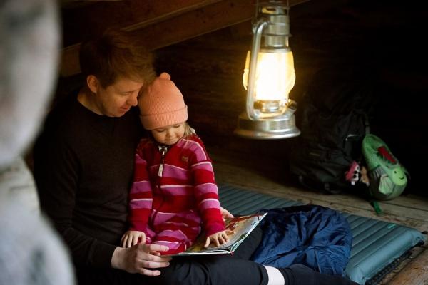 Isä ja lapsi lukevat kirjaa laavulla.