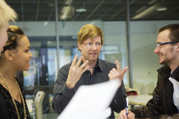 The teacher explains with her speech and hands to several students from different cultures.