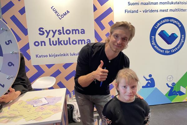 Kuvassa somevaikuttaja Satusetä faninsa Isabella Karvisen kanssa Turun kirjamessujen Lukuloman ja Lukutaito-ohjelman osastolla.