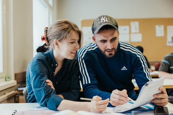 Kaksi henkilöä tutkii opiskelutehtävää luokkahuoneessa. 