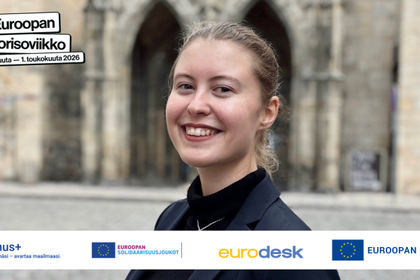 Nainen katsoo hymyillen kameraan. Hänellä on musta jakku päällä. Logot: Erasmus+, Euroopan solidaarisuusjoukot, Eurodesk, Euroopan unioni, Euroopan nuorisoviikko