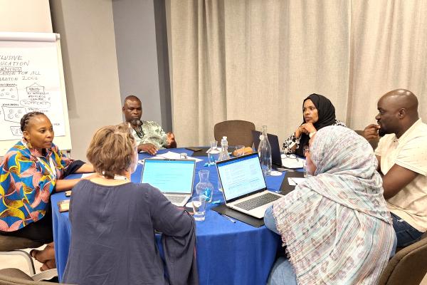 Six workshop participants are sitting together around a round table and working on a groupwork project in the workshop.