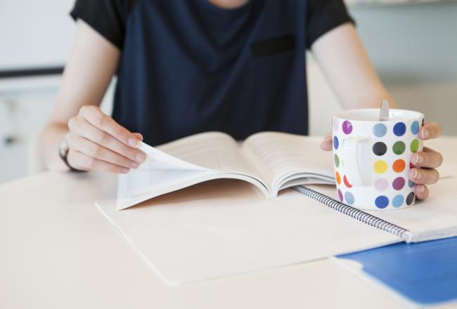 Kuvituskuva, nainen lukee lehteä ja juo kahvia