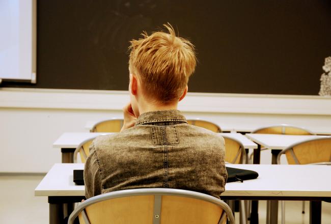 Opiskelija istuu luokkahuoneessa selin kuvaan