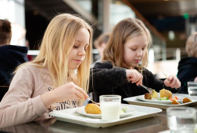 Kaksi tyttöä syövät vierekkäin ruokalassa