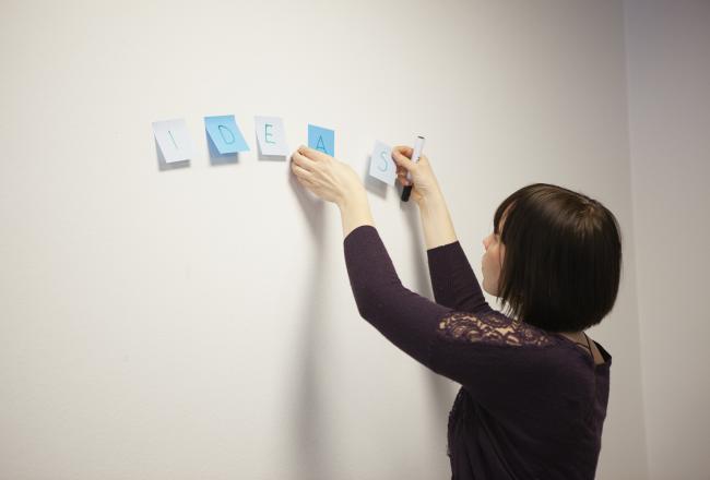 Kuvituskuva, nainen liimaa post-it lappuja seinälle