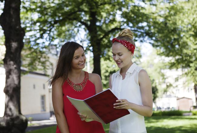Kuvituskuva, kaksi opiskelijaa lukee kirjaa ulkona