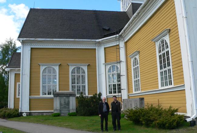 Ikaalisten käsi- ja taideteollisuusoppilaitoksen opettajat Heikki Jylhä-Vuorio ja Esko Huhtala Ikaalisten kirkon edustalla. Kirkon katon tervaaminen perinteiseen tapaan oli osa rakennusentisöinnin opiskelijoiden opintoja.