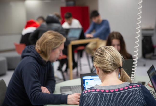 Opiskelijoita luokassa sivulta ja takaapäin kuvattuna.