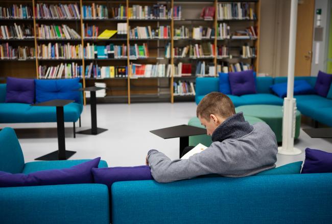 Mies sohvalla ammatillisen oppilaitoksen opiskelijakirjastossa selin kameraan