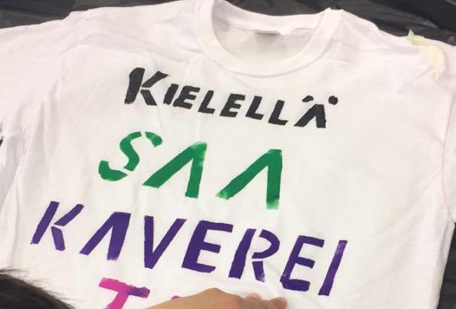 Valkoinen teepaita, johon oppilas on painanut värikkään tekstin jossa lukee: Kielellä saa kavereita