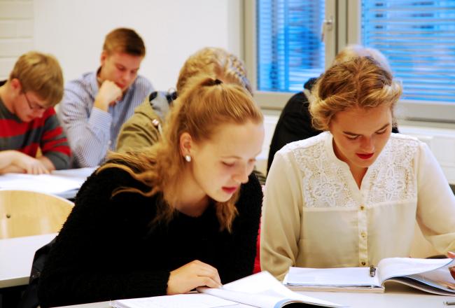 Oppilaita tunnilla pulpetin ääressä lukemassa oppikirjan tekstiä.