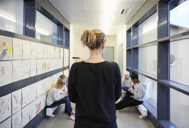 Opettaja seisoo koulun käytävällä selin kameraan