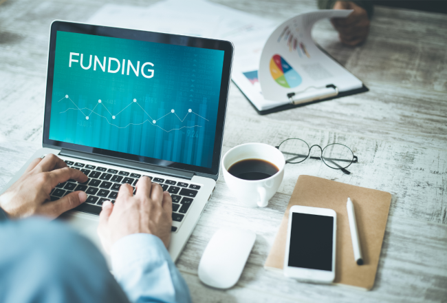 Händer och dator försedda med text Funding