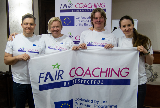 Kuvassa rivissä neljä ihmistä, pitelevät Fair Coaching -lippua. Kuvassa Suomen Fari Coaching -porukka Belgradin seminaarissa