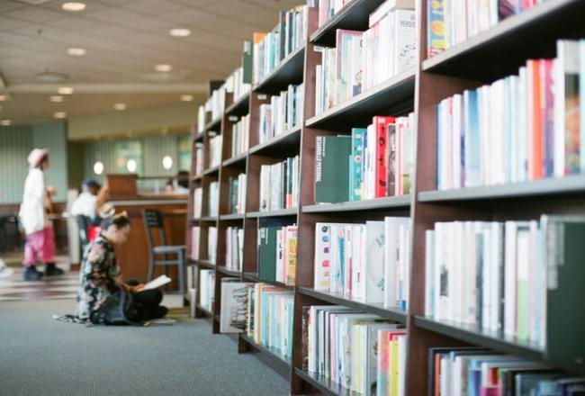 Woman reading a book in front of bookshelves. 