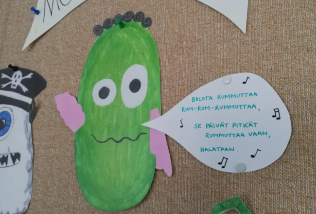 Kuvassa piirros vihreästä monsterista, joka laulaa.