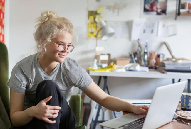 Nuori hymyilevä nainen kannettavan koneen edessä kotonaan