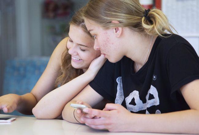 Kaksi nuorta nojaavat toisiinsa ja katsovat puhelinta.