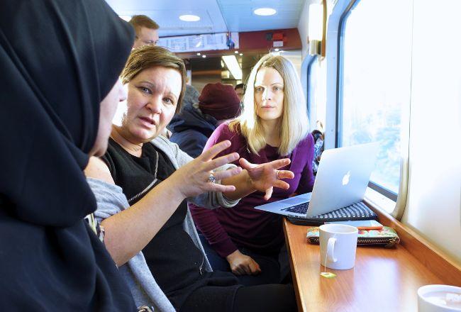 Kolme henkilöä keskustelee kannettavan tietokoneen äärellä junassa.