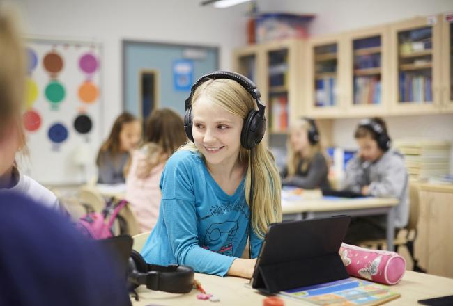 Vaaleahiuksinen lapsi hymyilee kuulokkeet korvillaan.