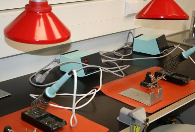 Kuvituskuva. Elektroniikkatöiden alueella työskennellään juotosaseman äärellä. Kohdepoiston imun tulee kohdistua juotoksesta syntyvien savukaasujen poistoon.