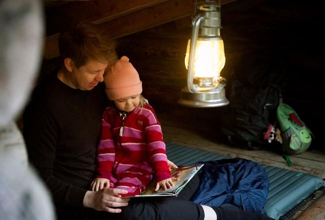 Isä ja lapsi lukevat kirjaa laavulla.