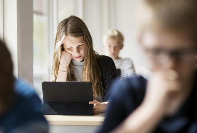 Opiskelija katsoo tablet-tietokonetta luokassa.