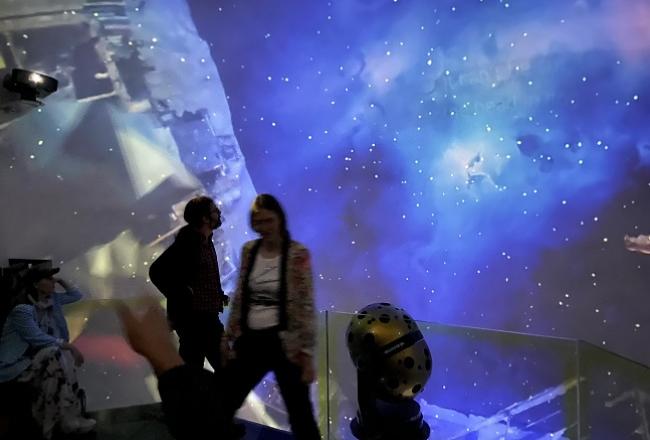 Tapahtuman osallistujia Tarton planetaariossa, taustalla sinivioletti avaruuskuva