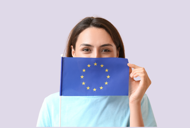 Nainen pitää kasvojensa edessä EU-lippua ja kurkistaa sen takaa.