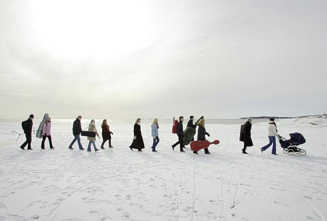 Ryhmä orkesterimuusikoita kävelee talvisella merenjäällä instrumenttilaukkuja kantaen.
