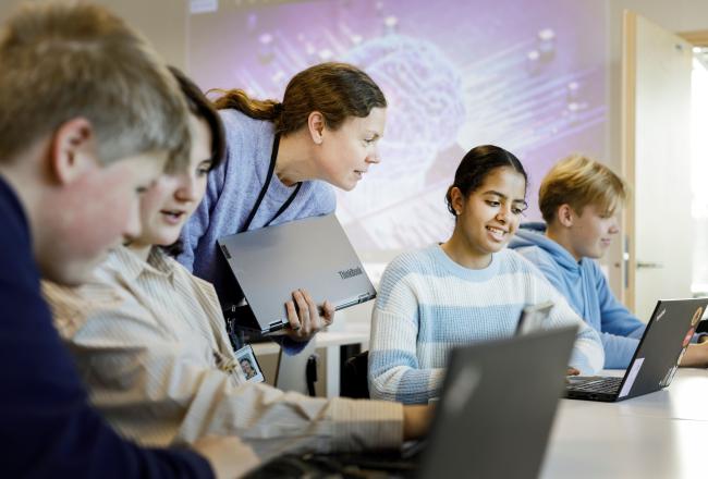 Oppilaat  vieretysten, opettaja katsoo oppilaan tietokoneen näyttöä