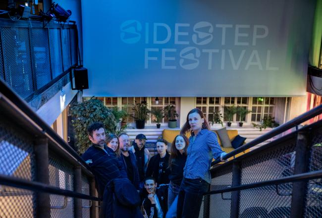 Kuvassa joukko ihmisiä portaikossa ja heidän takanaan teksti Sidestep Festival