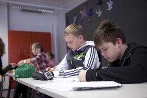 Kuvituskuva, pojat kirjoittavat pöydän ääressä