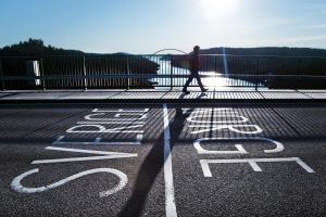 Ihminen kävelee jalkakäytävällä auringon paisteessa, Ruotsin ja Norjan rajan yli.