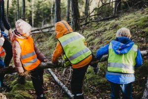 Lapsia metsässä kiipeilemässä puunrungon päällä.