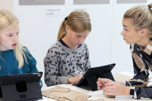 Opettaja ohjaa oppilaita, jotka työskentelevät tableteilla