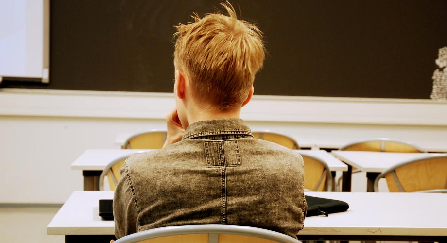 Opiskelija istuu luokkahuoneessa selin kuvaan