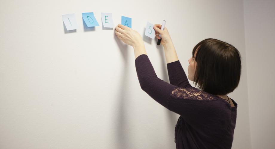Kuvituskuva, nainen liimaa post-it lappuja seinälle