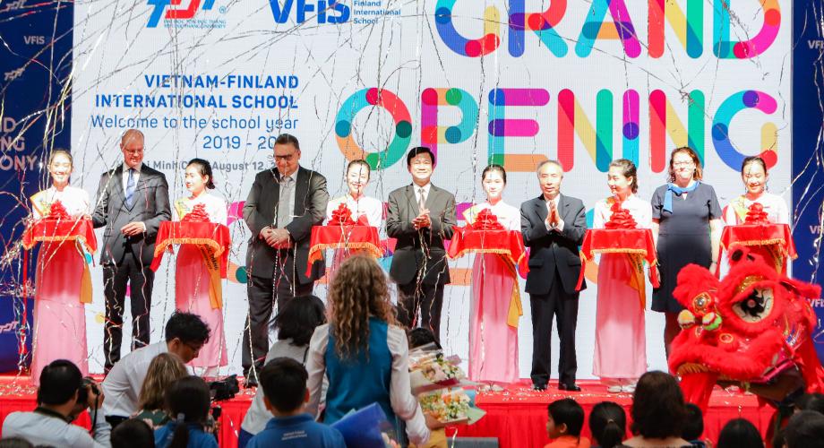 Finnish and Vietnamese official standing on a stage, ready to cut a ceremonial cord held by women dressed in traditional Vietnamese costume.