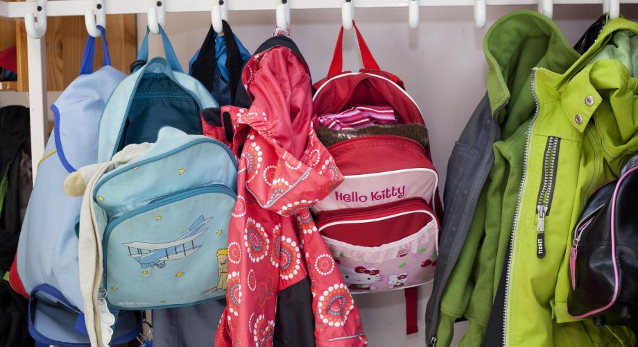 Colourful school bags hanging in a clothes rack in the school corridor