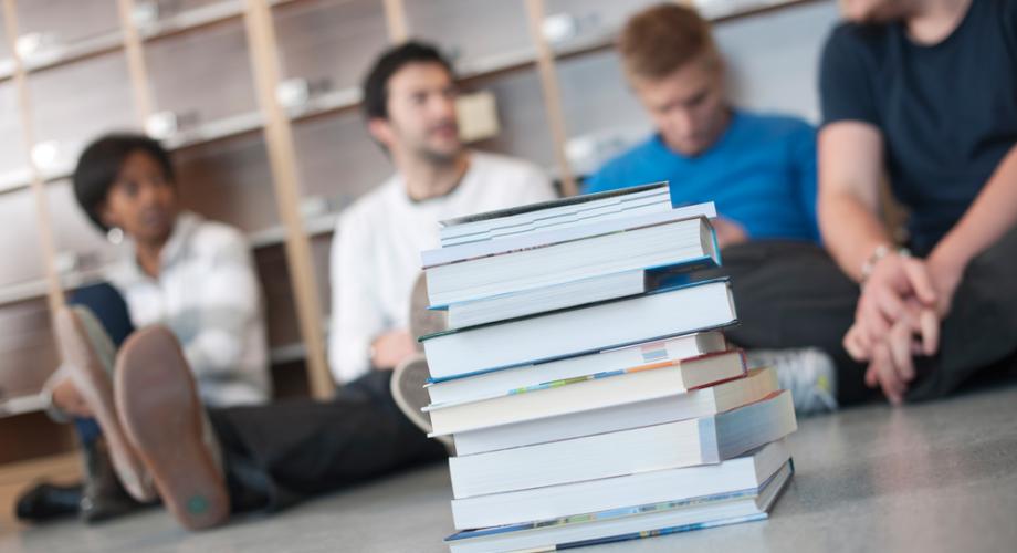 Pile of study books in the foreground and some students sitting at the background