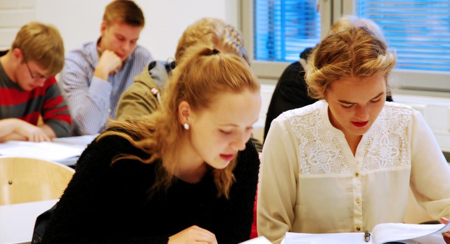 Oppilaita tunnilla pulpetin ääressä lukemassa oppikirjan tekstiä.