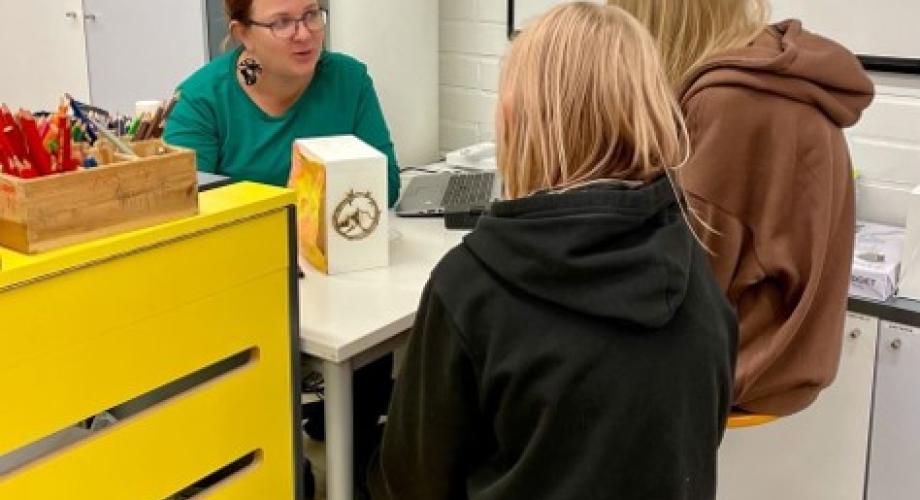 Kuvituskuva: Opettaja pitää käsityön arviointikeskustelua kahden oppilaan kanssa. Tarkastelun alla oppimiskokonaisuudessa tehty käsityötuote ja siihen liittyvä prosessi.