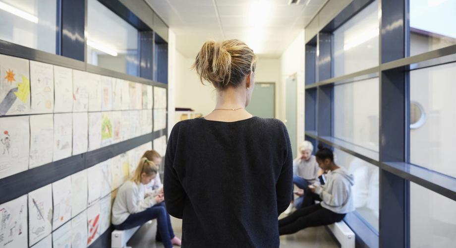 Opettaja seisoo koulun käytävällä selin kameraan