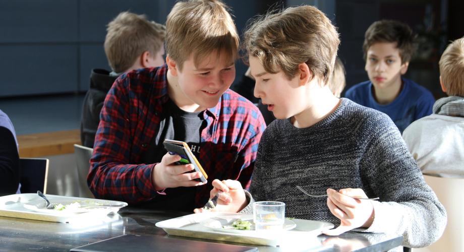 Pojat katsovat yhdessä kännykkää ruokalassa.