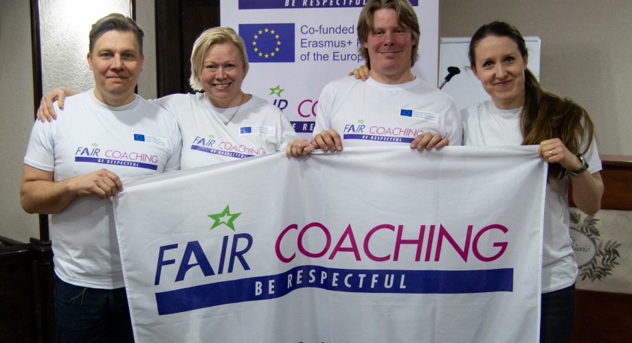 Kuvassa rivissä neljä ihmistä, pitelevät Fair Coaching -lippua. Kuvassa Suomen Fari Coaching -porukka Belgradin seminaarissa