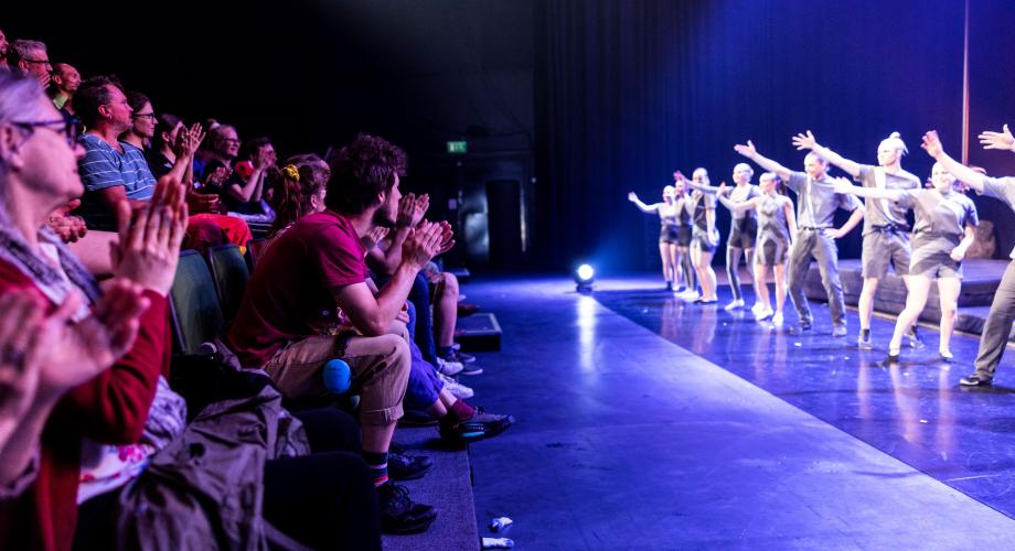 Circus performers waiving hands, audience clapping.