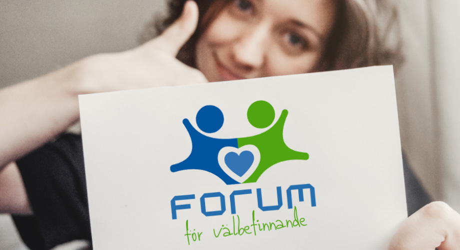En person ger tummen upp samtidigt som hen håller upp en skylt med texten: Forum för välbefinnande